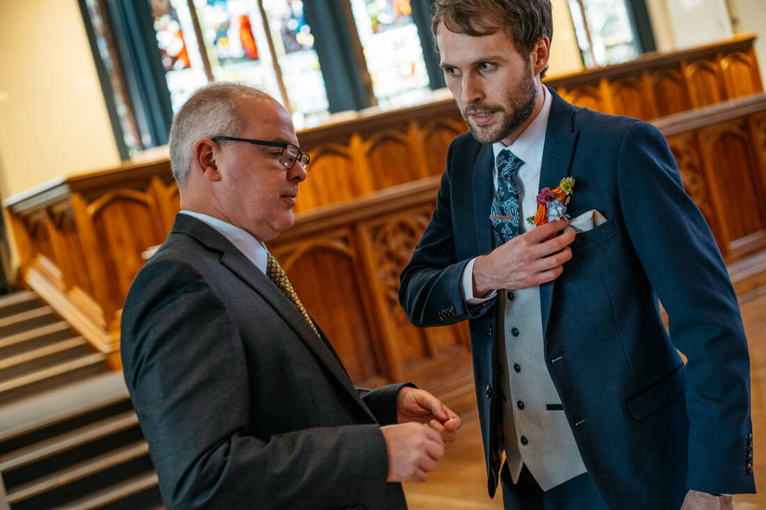 groom, jack, fixes his buttonhole amidst the stunning interior of Guildhall, with stain glassed windows and organ starting to fill with guests, a breathtaking scene captured by Patrick Duddy, before heading to the Bishops Gate Hotel for the celebration in Derry.