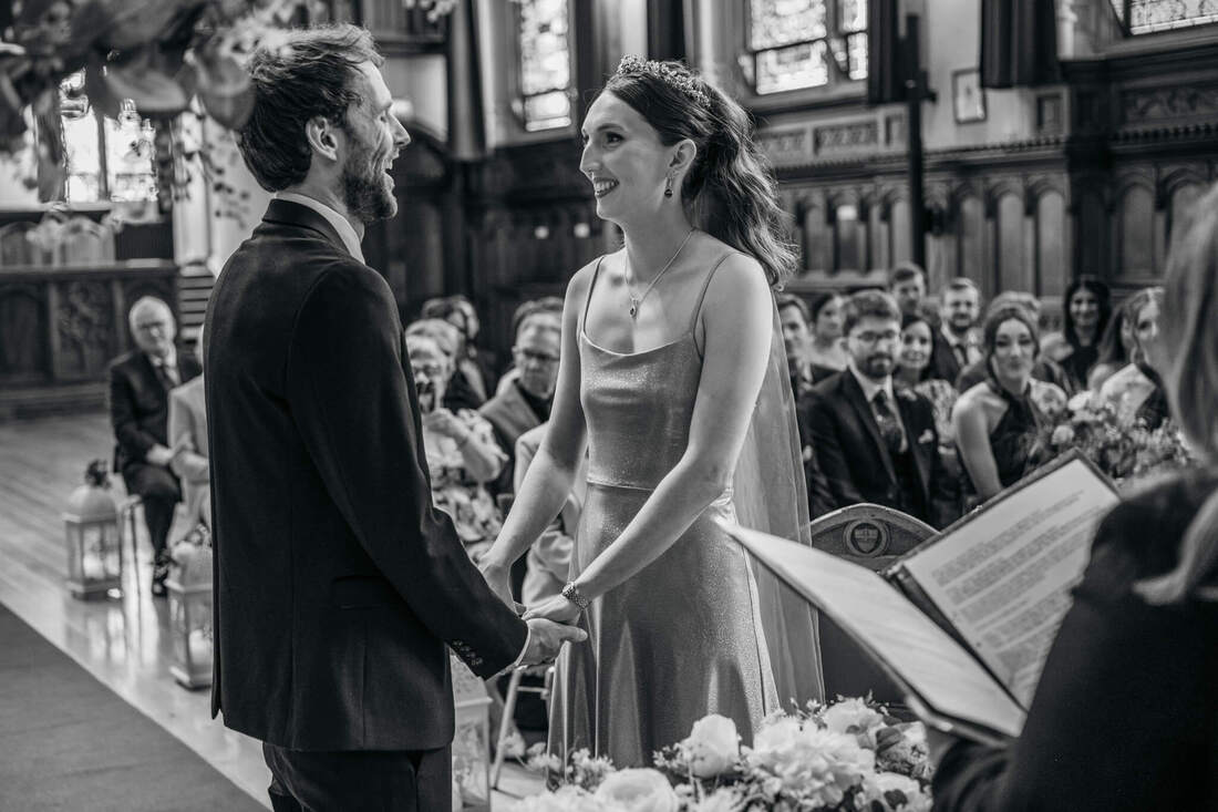 Claire and Jack holding hands during the ceremony at Guildhall, a touching moment captured by Patrick Duddy, before the reception at Bishops Gate Hotel in Derry in black and white